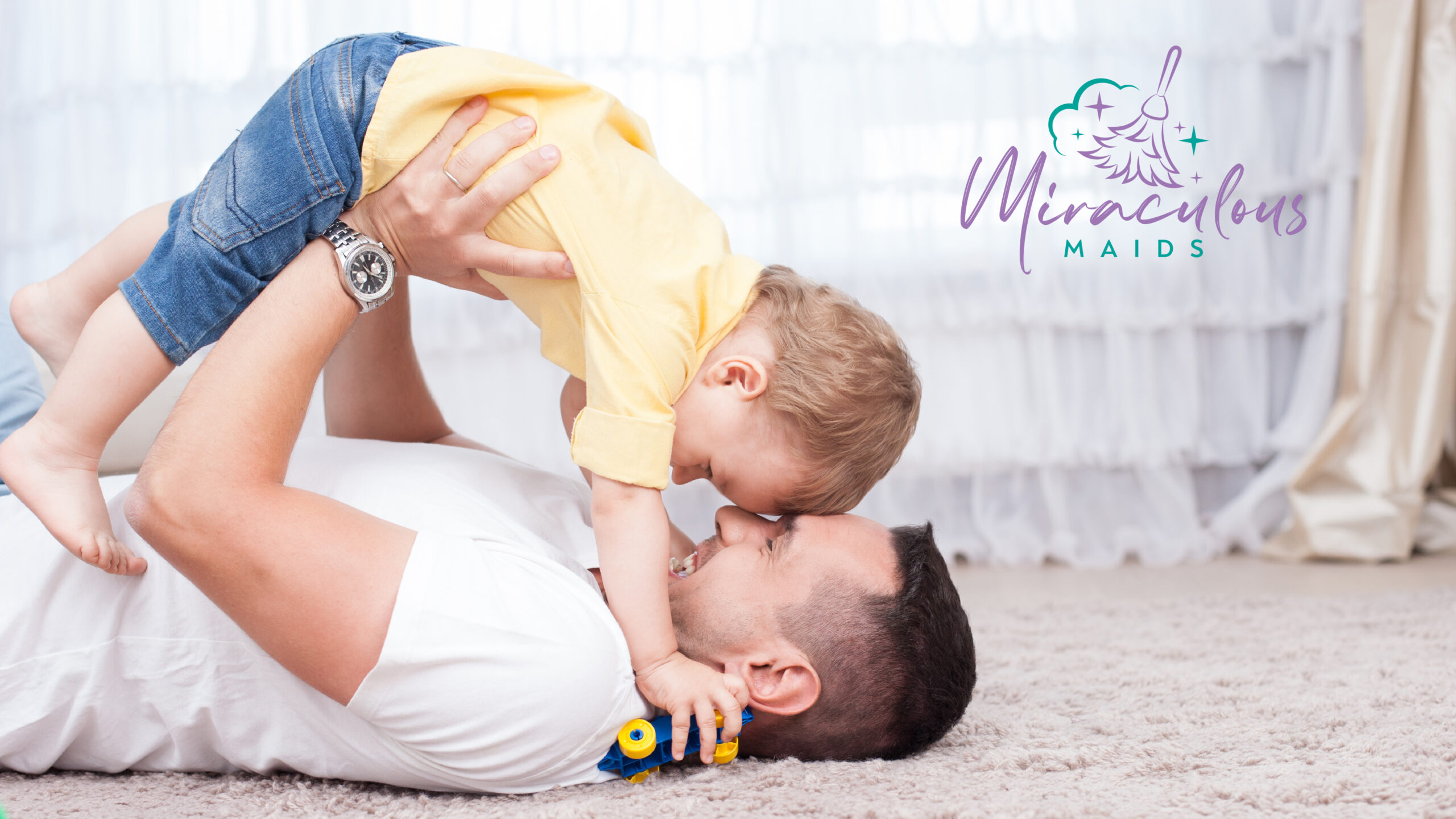 dad holding up little baby and laying on carpet with Miraculous Maids logo