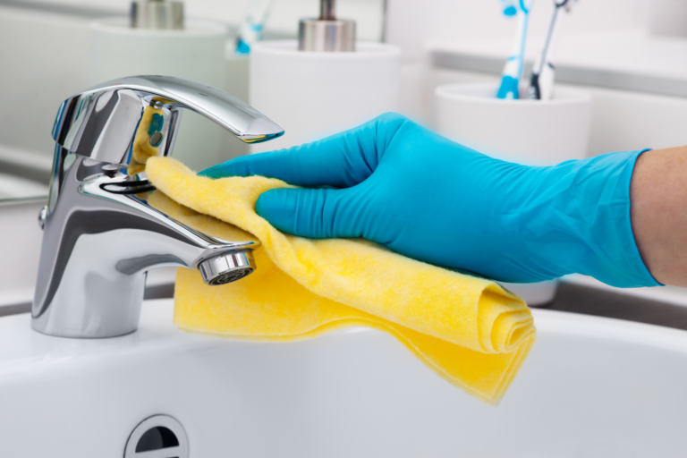 person cleaning bathroom tap with yellow cloth and blue gloves