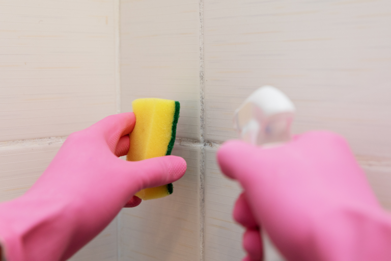 person cleaning grout tile with scrubby brush wearing pink gloves